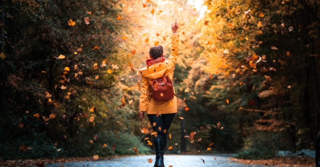 Person walking down a road with fall leaves falling